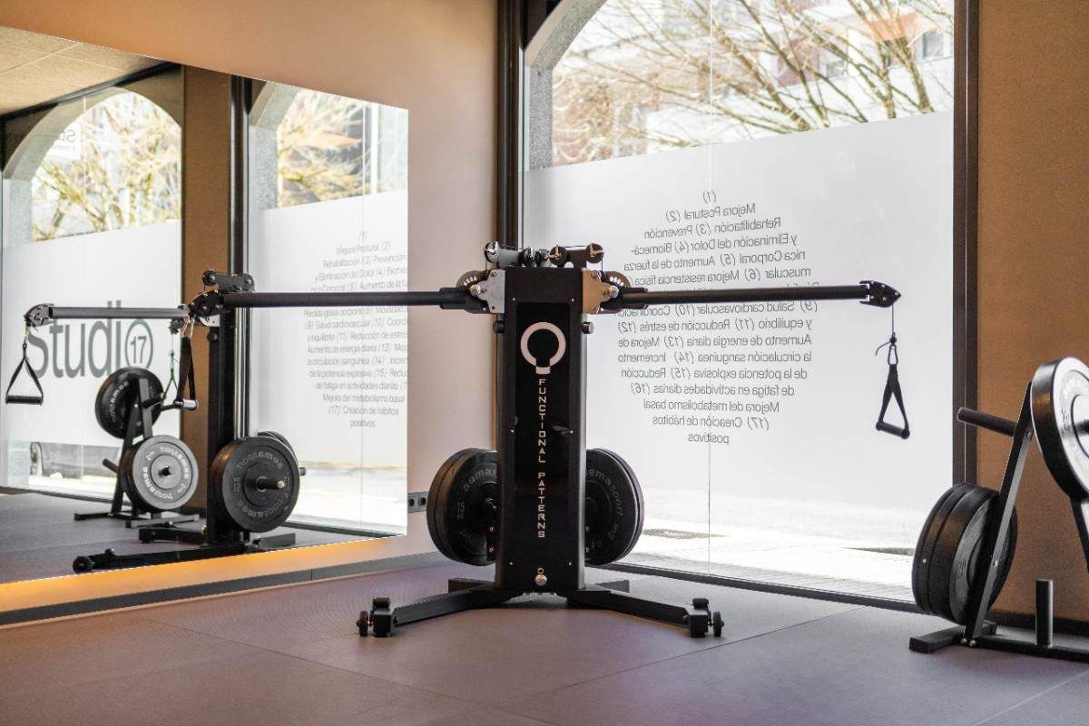 Gimnasio con aparatos que incluyen cinta de correr y pesas, con un gran espejo y decoración en tonos neutros.