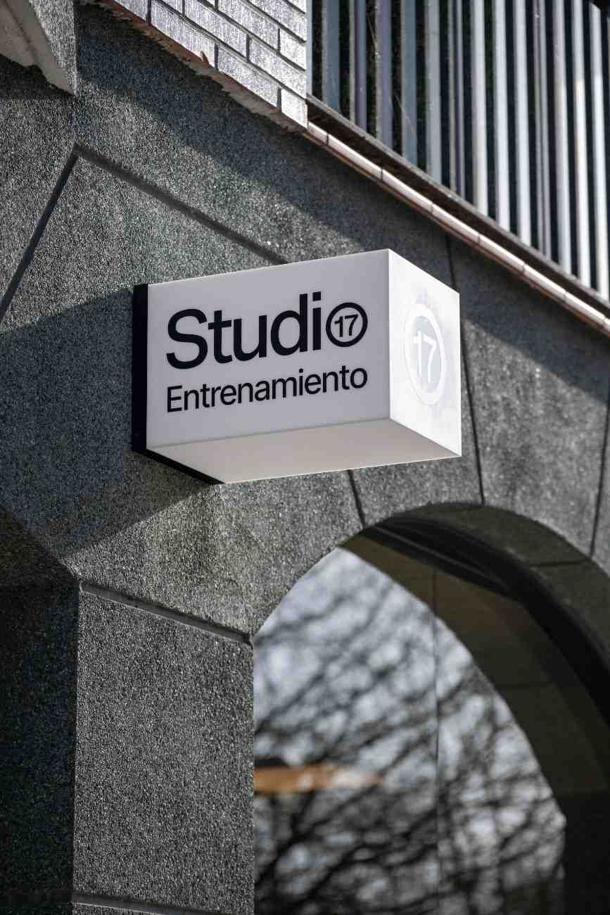 Letrero para "Studio 17 Entrenamiento", caja blanca con letras negras, montado sobre una pared texturizada gris con arco.