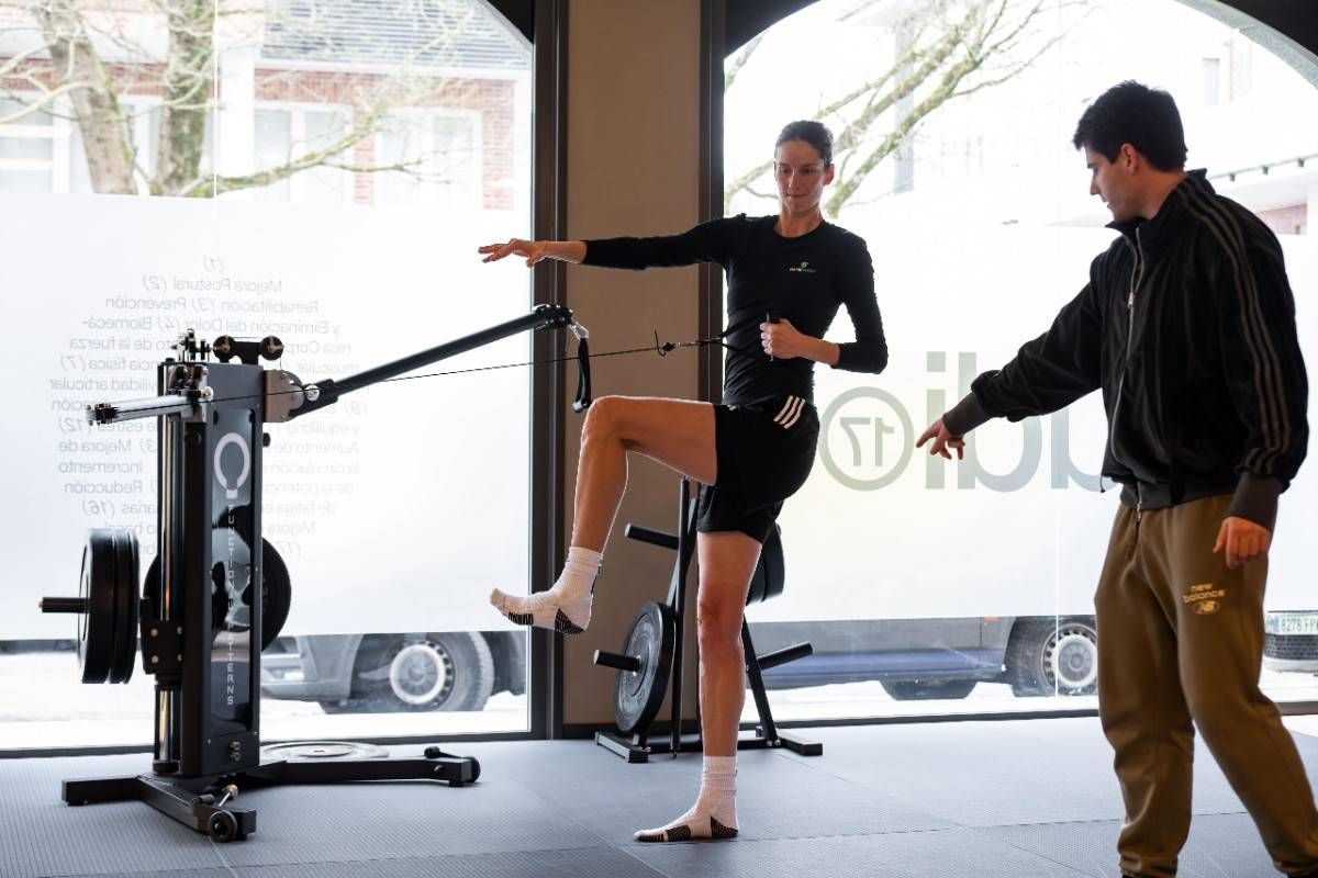 Gimnasio con aparatos que incluyen cinta de correr y pesas, con un gran espejo y decoración en tonos neutros.