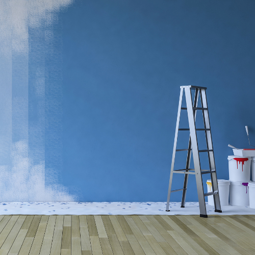 Une échelle est dressée contre un mur bleu partiellement peint en blanc. Des seaux de peinture et des pinceaux sont posés.
