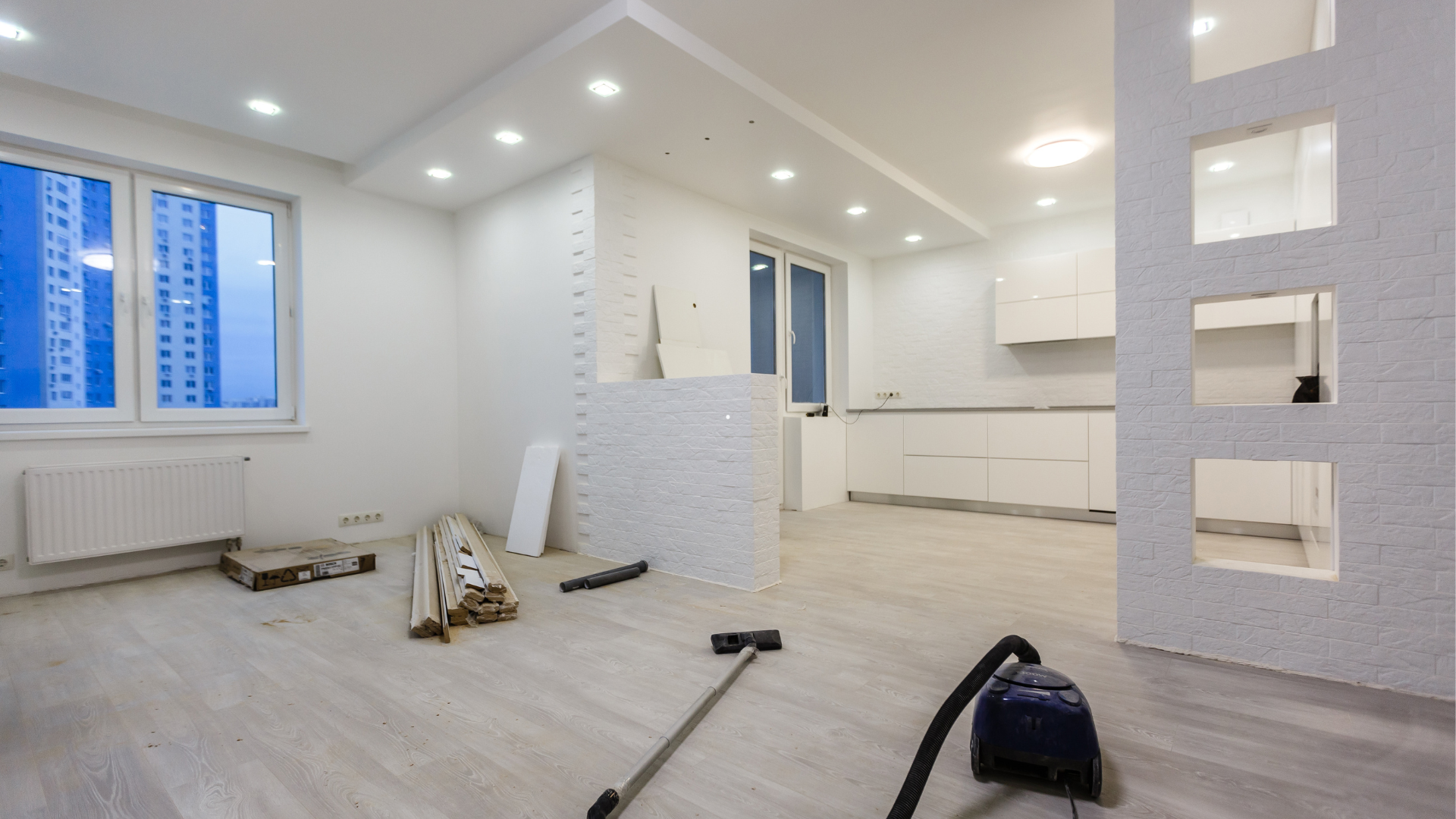 Rénovation en cours : intérieur blanc lumineux avec murs apparents, nouveau revêtement de sol et aspirateur dans la pièce.