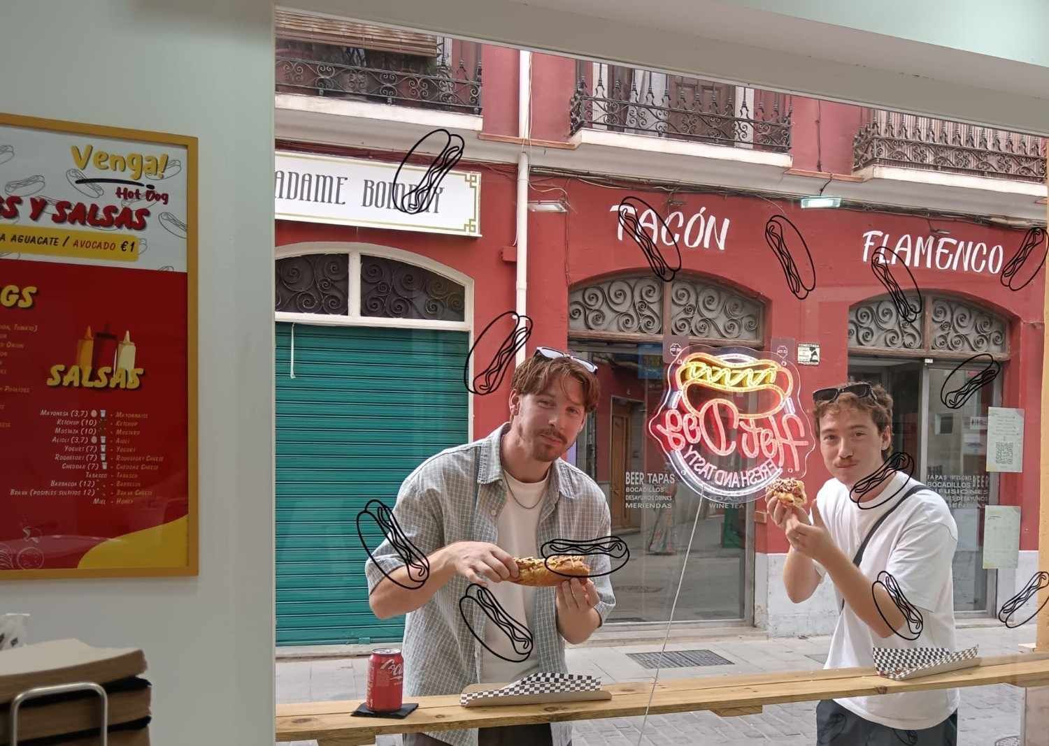 Dos hombres comiendo perritos calientes en la ventana de un restaurante. Un edificio rojo detrás de ellos.
