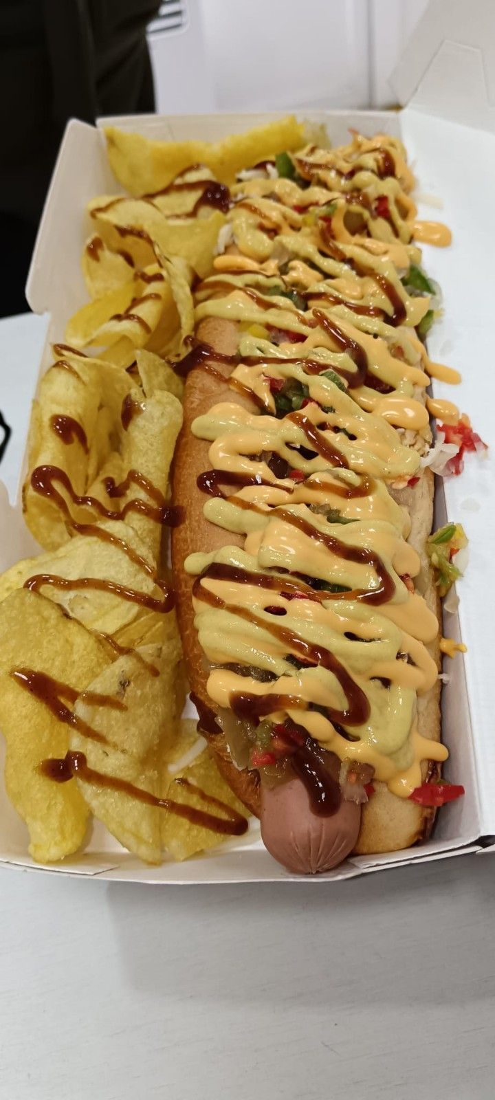 Perro caliente con salsa y patatas fritas en envase para llevar.