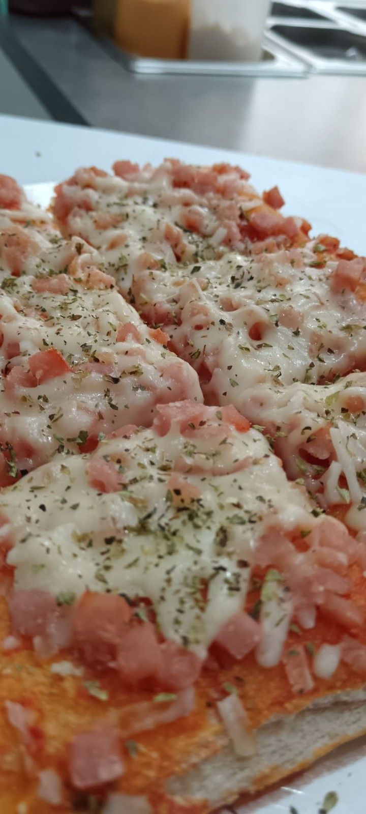 Porciones de pizza con queso derretido, tomates picados y hierbas sobre una superficie blanca.