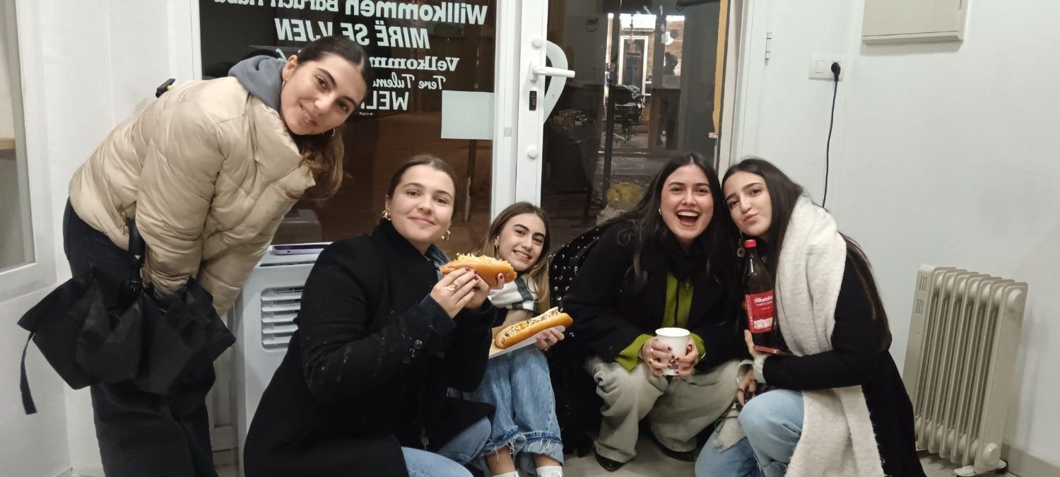 Cinco jóvenes sonríen y posan cerca de una puerta. Dos sostienen comida y uno, una taza.