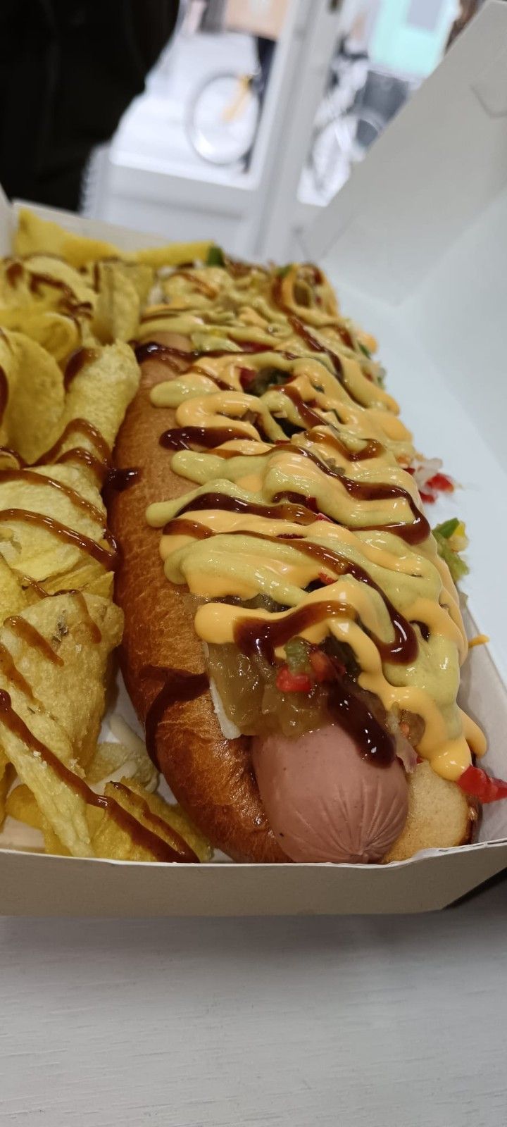 Perro caliente en caja con patatas fritas, cubierto de salsa y aderezos.