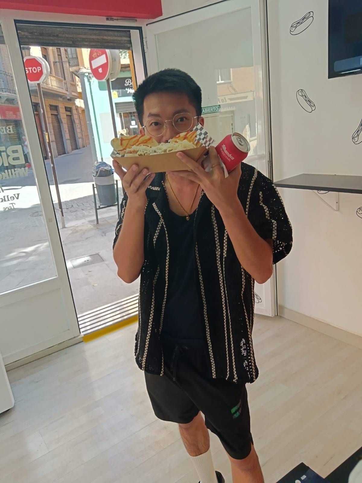 Persona sosteniendo un sándwich grande y un refresco dentro de la puerta de un restaurante.