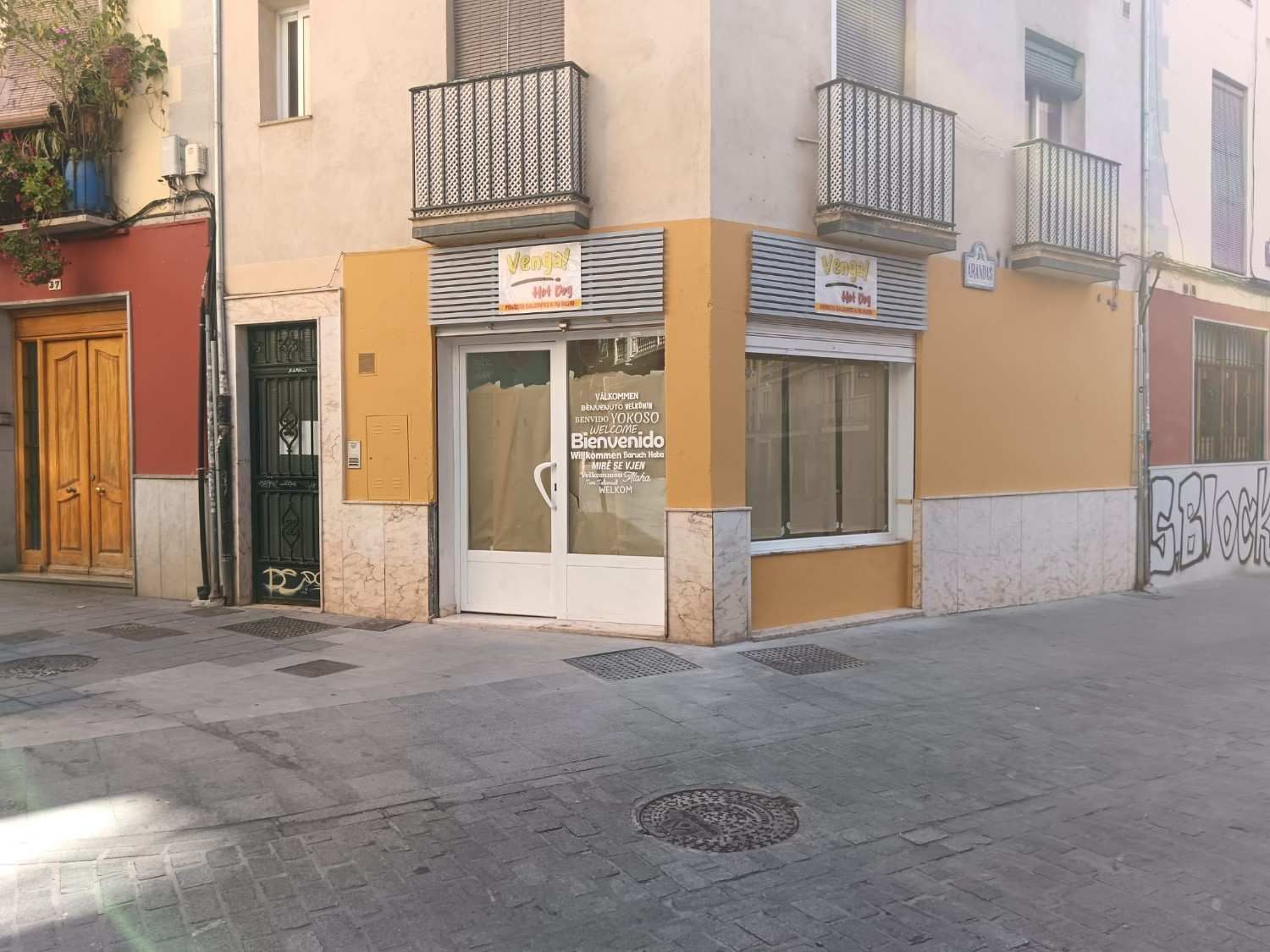 Edificio esquinero con local comercial, dos balcones y puerta cerrada a calle de ciudad.