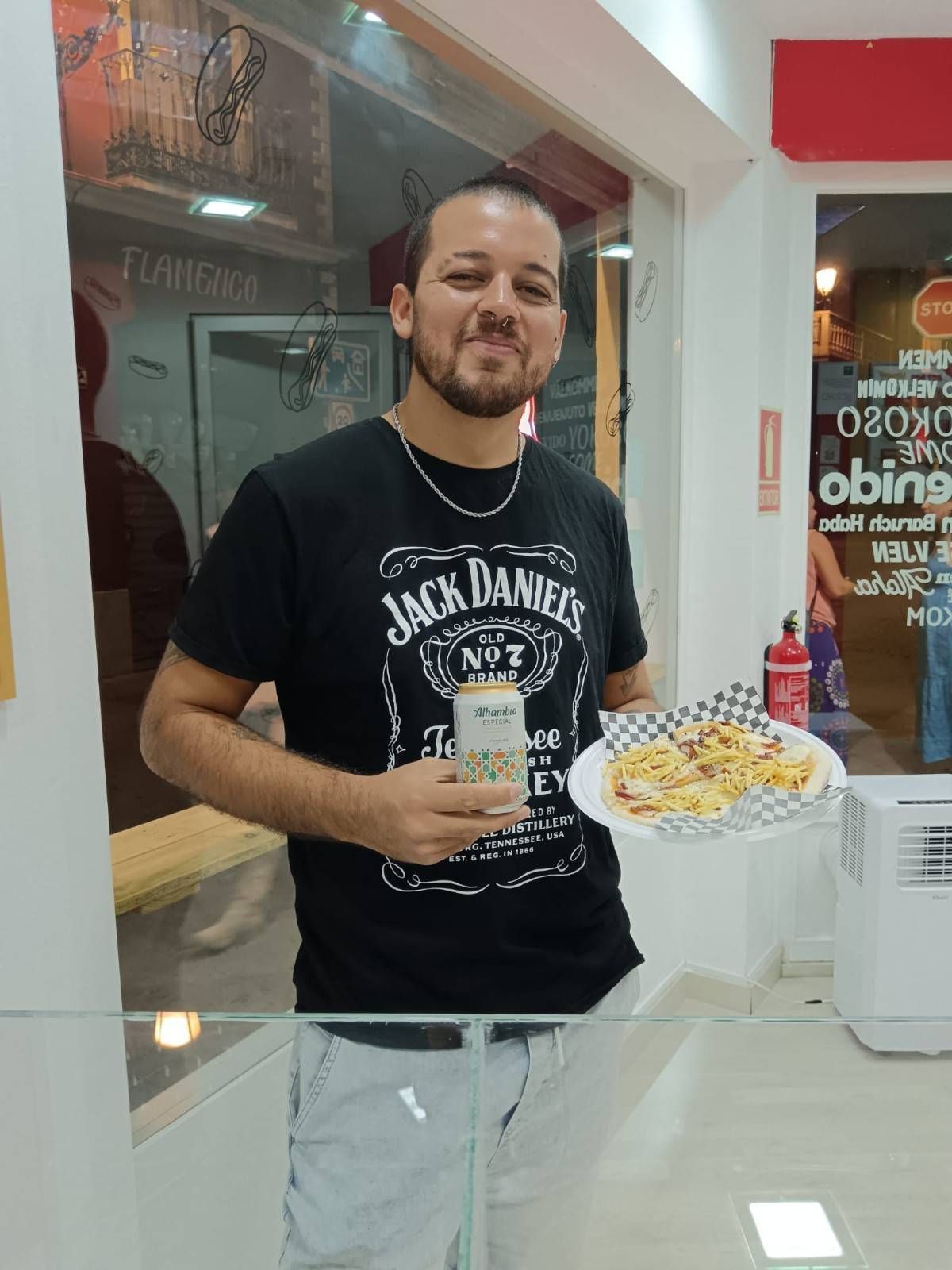 Hombre con camiseta de Jack Daniel's sosteniendo comida y una bebida en una tienda.