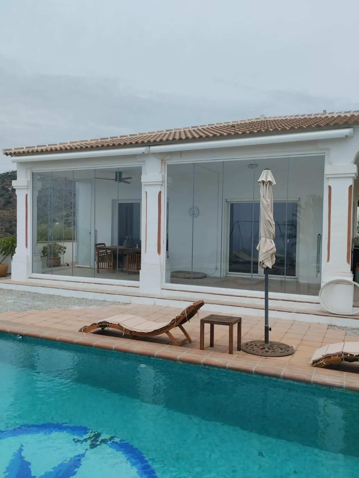 Villa moderna con piscina, tumbonas y patio embaldosado junto al agua.