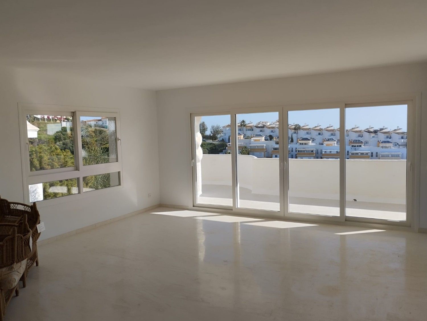 Sala de estar luminosa y vacía con grandes ventanales con vistas a un puerto deportivo.