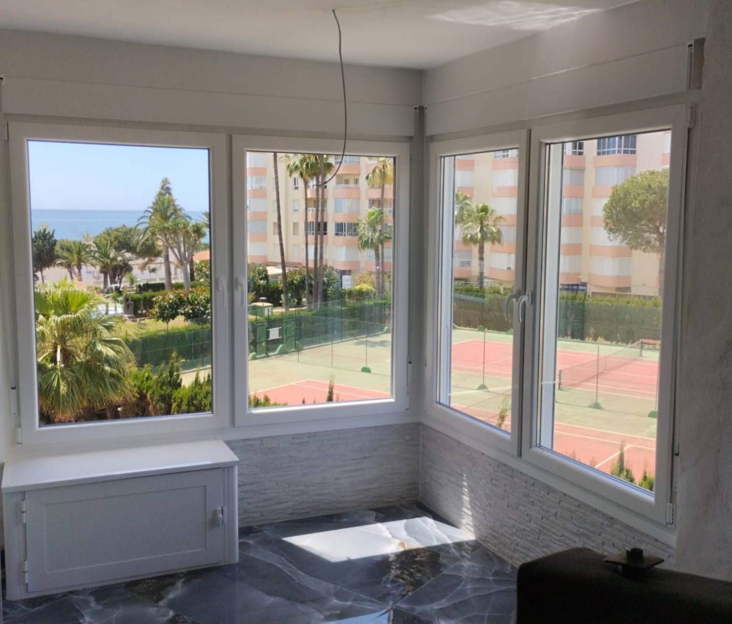 Habitación luminosa en esquina con grandes ventanales con vistas a las pistas de tenis y a las palmeras junto al mar.