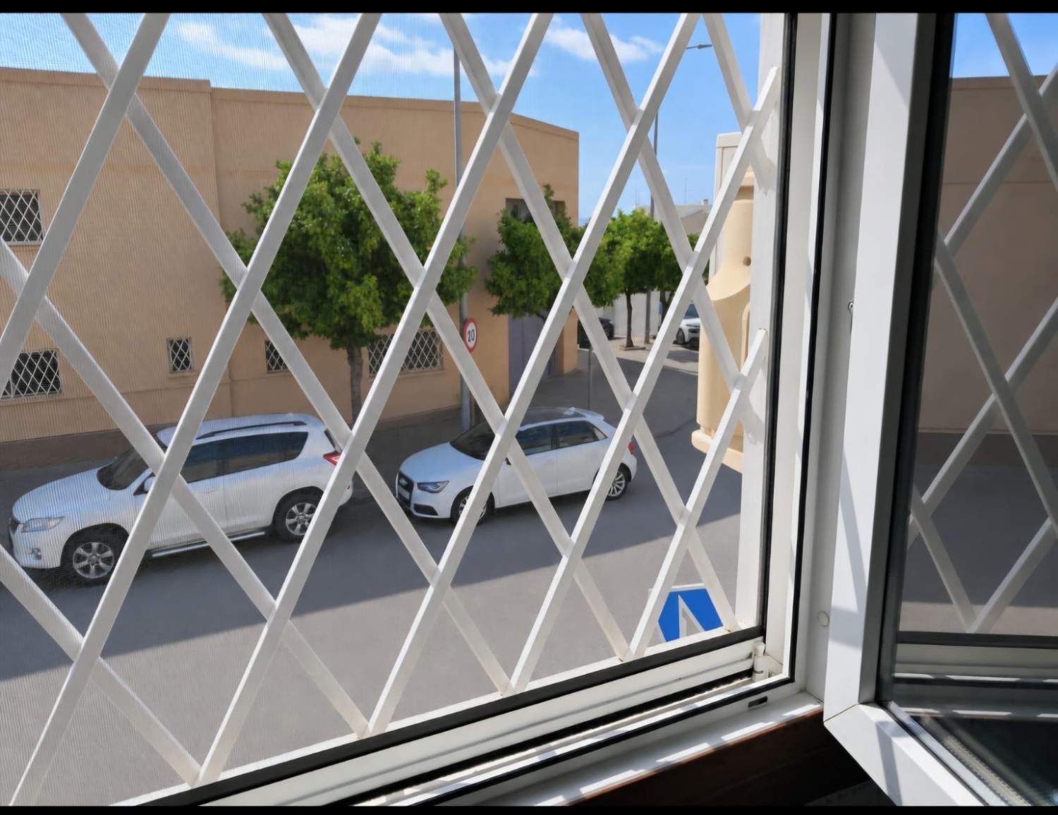 Habitación luminosa y vacía con grandes ventanales, paredes blancas y vistas a árboles y edificios en el exterior.