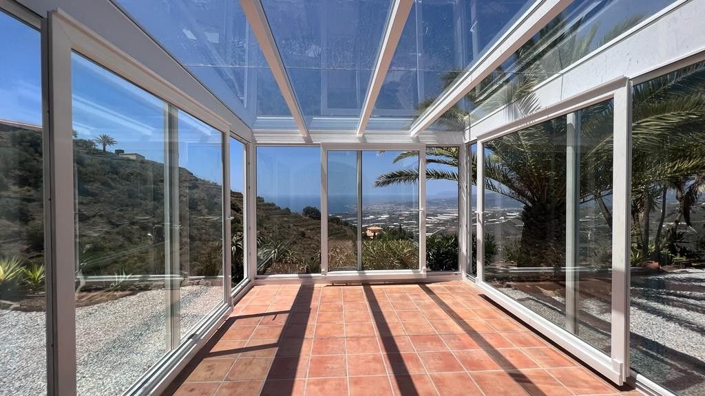 Terraza acristalada con suelo de baldosas de terracota y vistas panorámicas a la montaña.