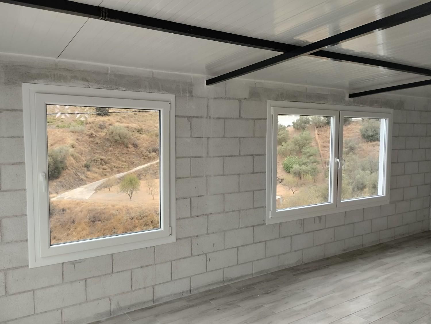 Habitación vacía con paredes de bloques de hormigón blanco, dos ventanas y vigas de techo negras a la vista.