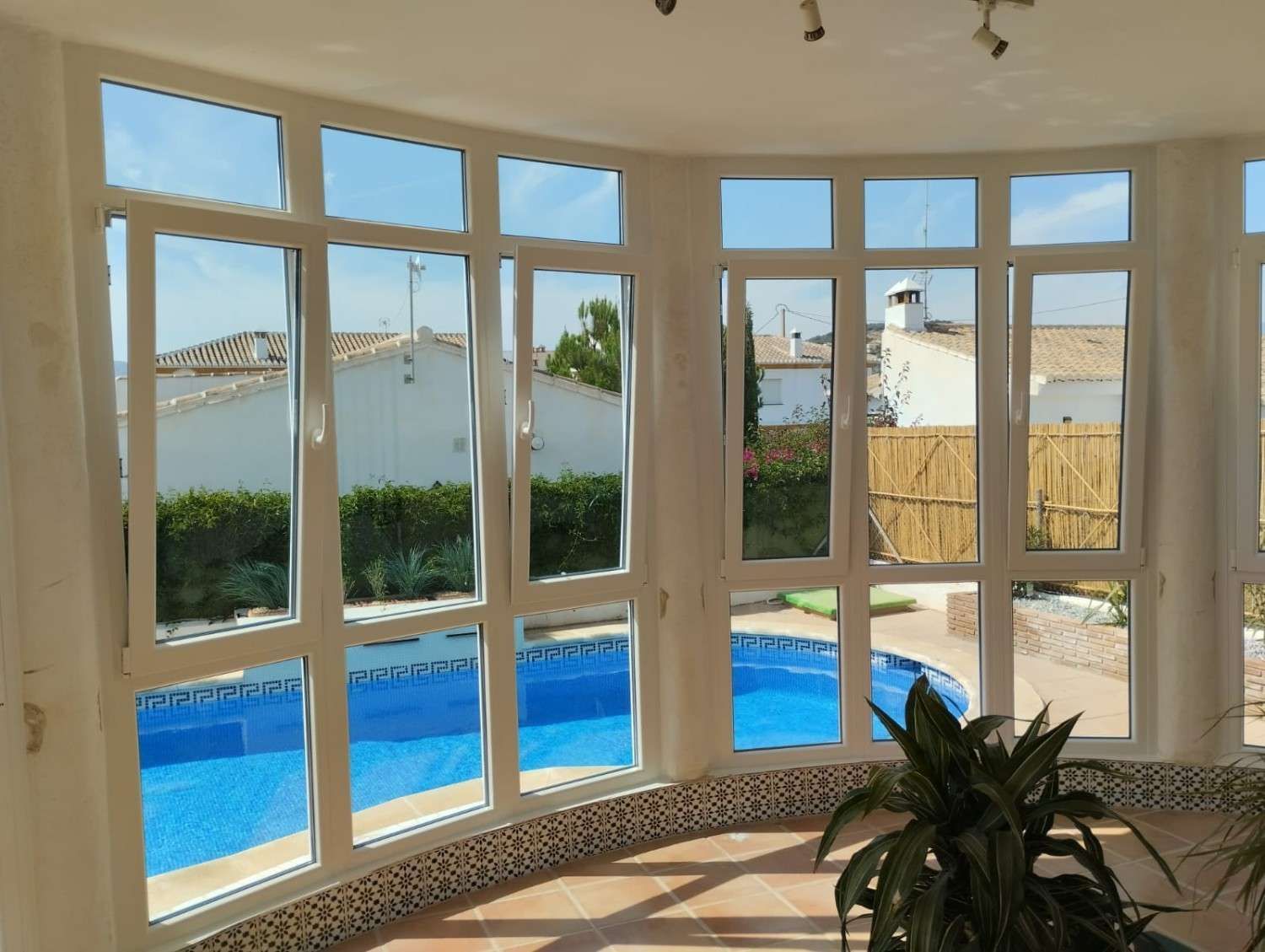 Luminoso solárium con ventanas de marcos blancos con vistas a una piscina azul y al océano.