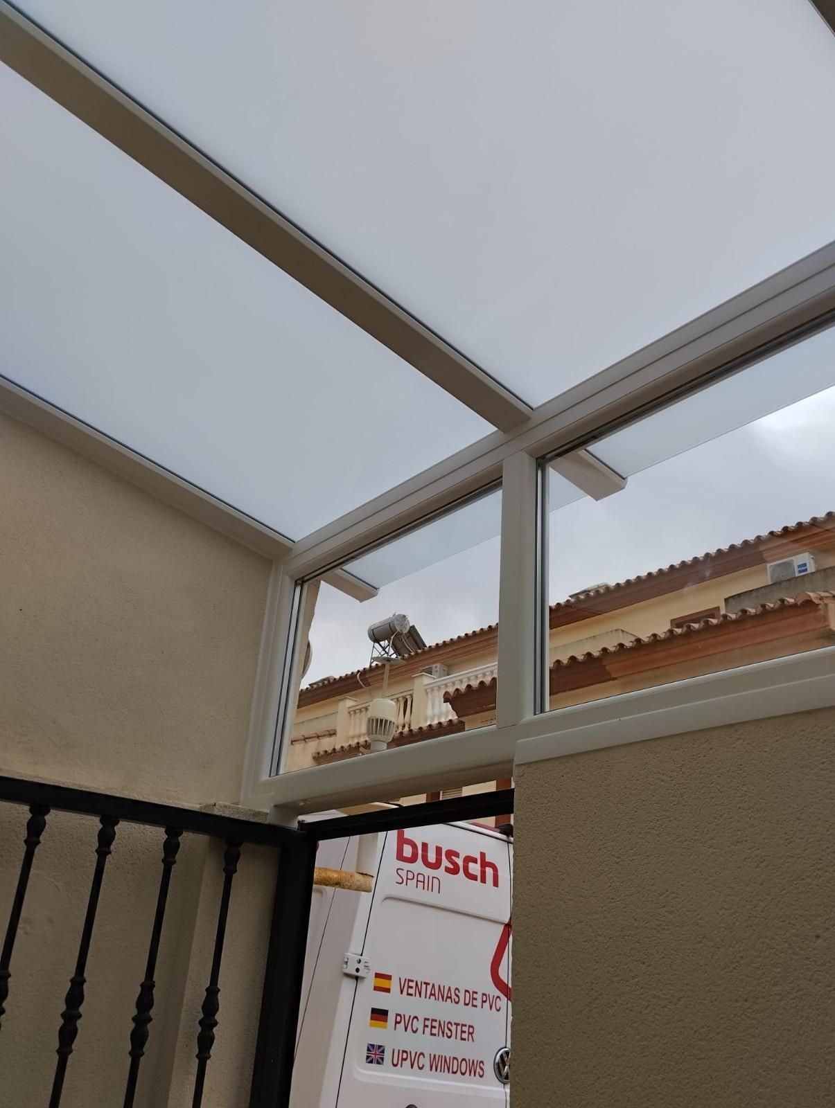 Estructura de techo de patio cubierto con paneles blancos, paredes beige y un letrero visible a través de la abertura.