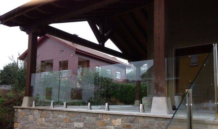 Casa moderna con grandes paredes de cristal y un patio de piedra bajo un alero de madera.