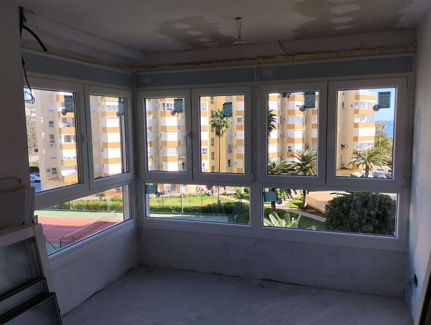Porche cerrado vacío con grandes ventanales con vistas a edificios de apartamentos y zonas verdes.