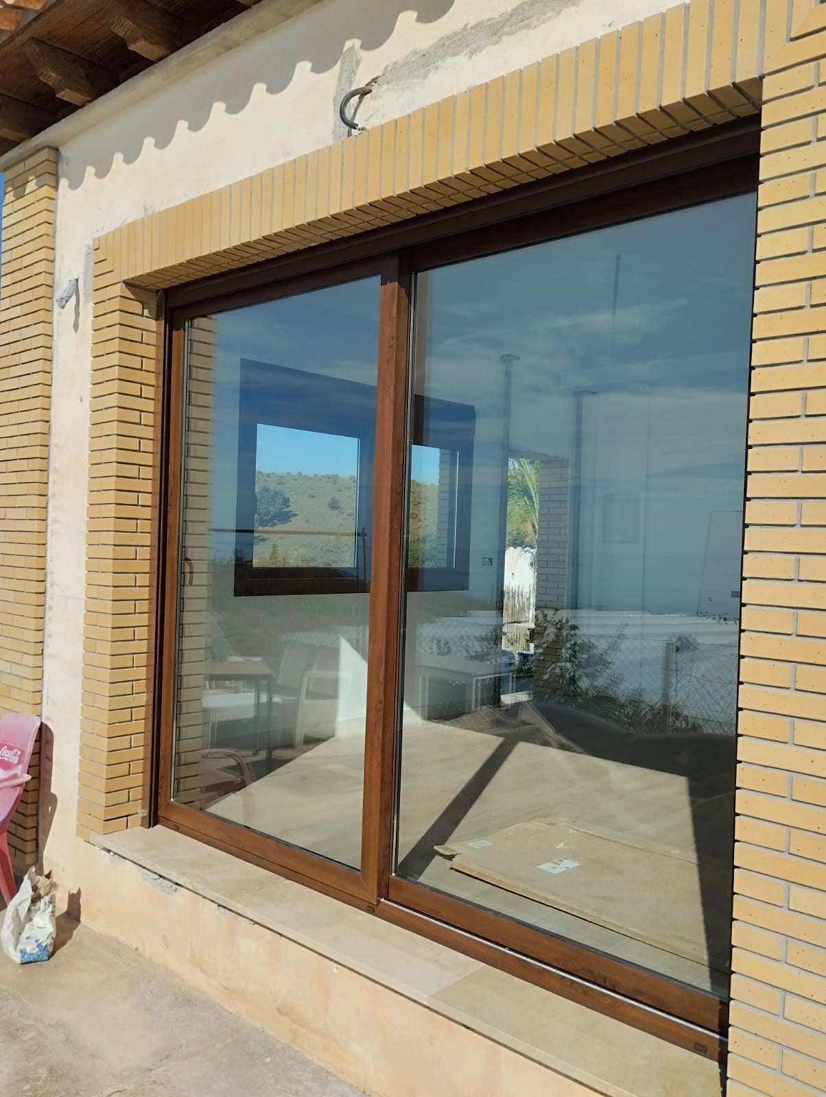 Gran puerta corrediza de cristal con marco marrón en una pared exterior de ladrillo color canela, que refleja las vistas al exterior.