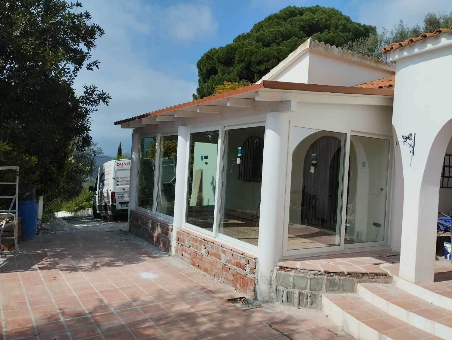 Casa blanca con porche arqueado y pasarela de baldosas rojas bajo los árboles, vista desde el lateral.