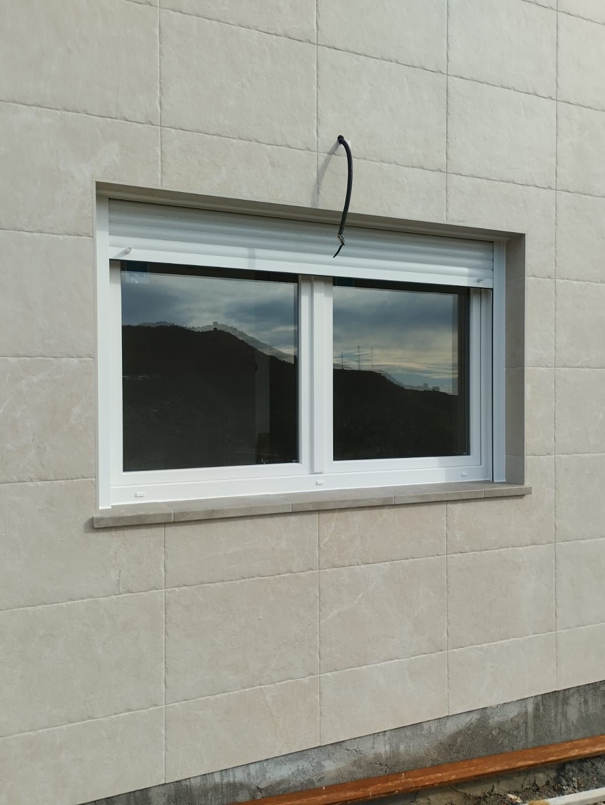 Ventana blanca enmarcada en una pared de azulejos beige con un cable negro colgando encima.