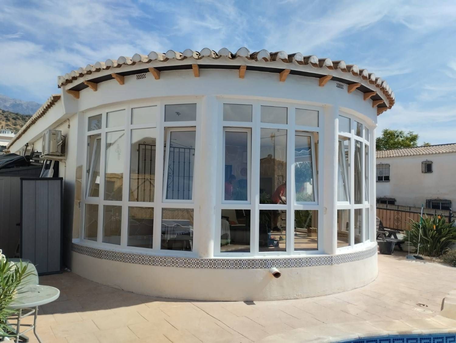 Terraza acristalada curva de color blanco con grandes ventanales y patio, vista a plena luz del día.