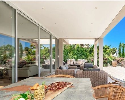 Patio moderno con asientos de mimbre, una mesa de comedor y una luminosa vista al exterior a través de puertas corredizas de vidrio.