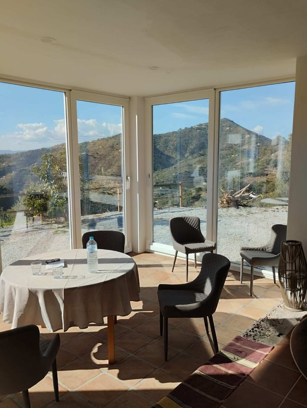 Cafetería soleada con mesas y sillas junto a grandes ventanales con vistas a la montaña.