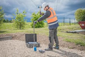 Technicien en position de travail qui tape sur une tige afin de connaître la profondeur jusqu'au refus du sol