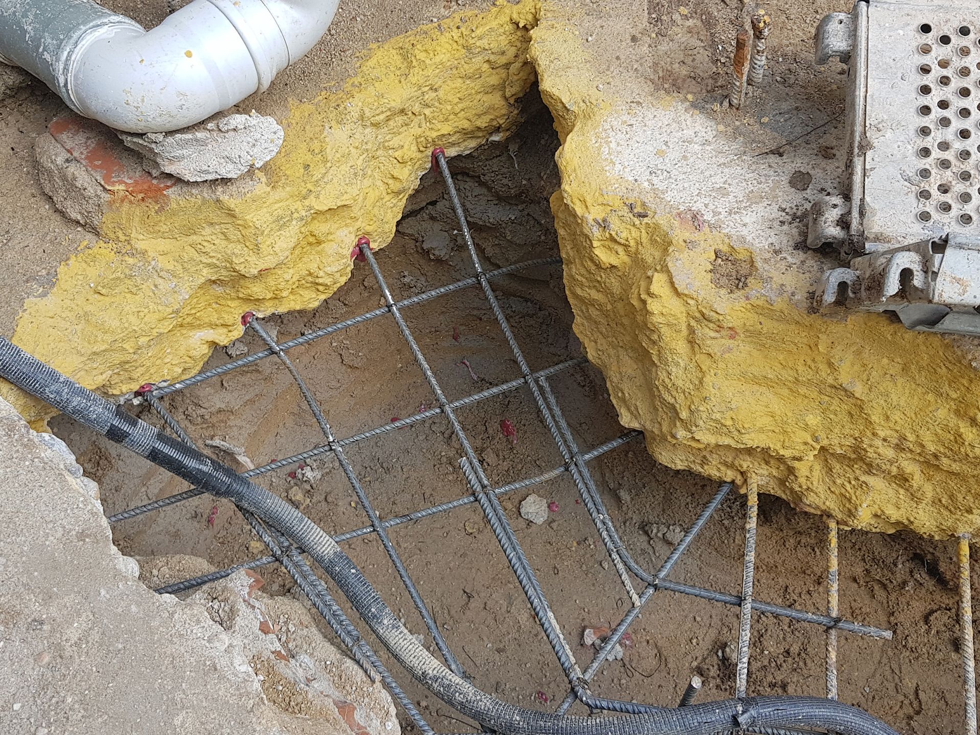 Un agujero en el suelo del que salen una tubería y cables.