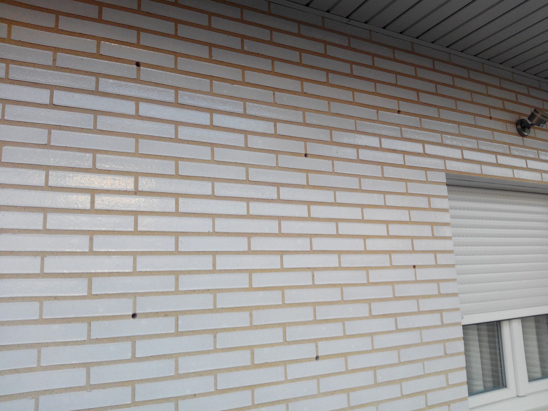 Una pared de ladrillo blanco con una ventana y contraventanas.