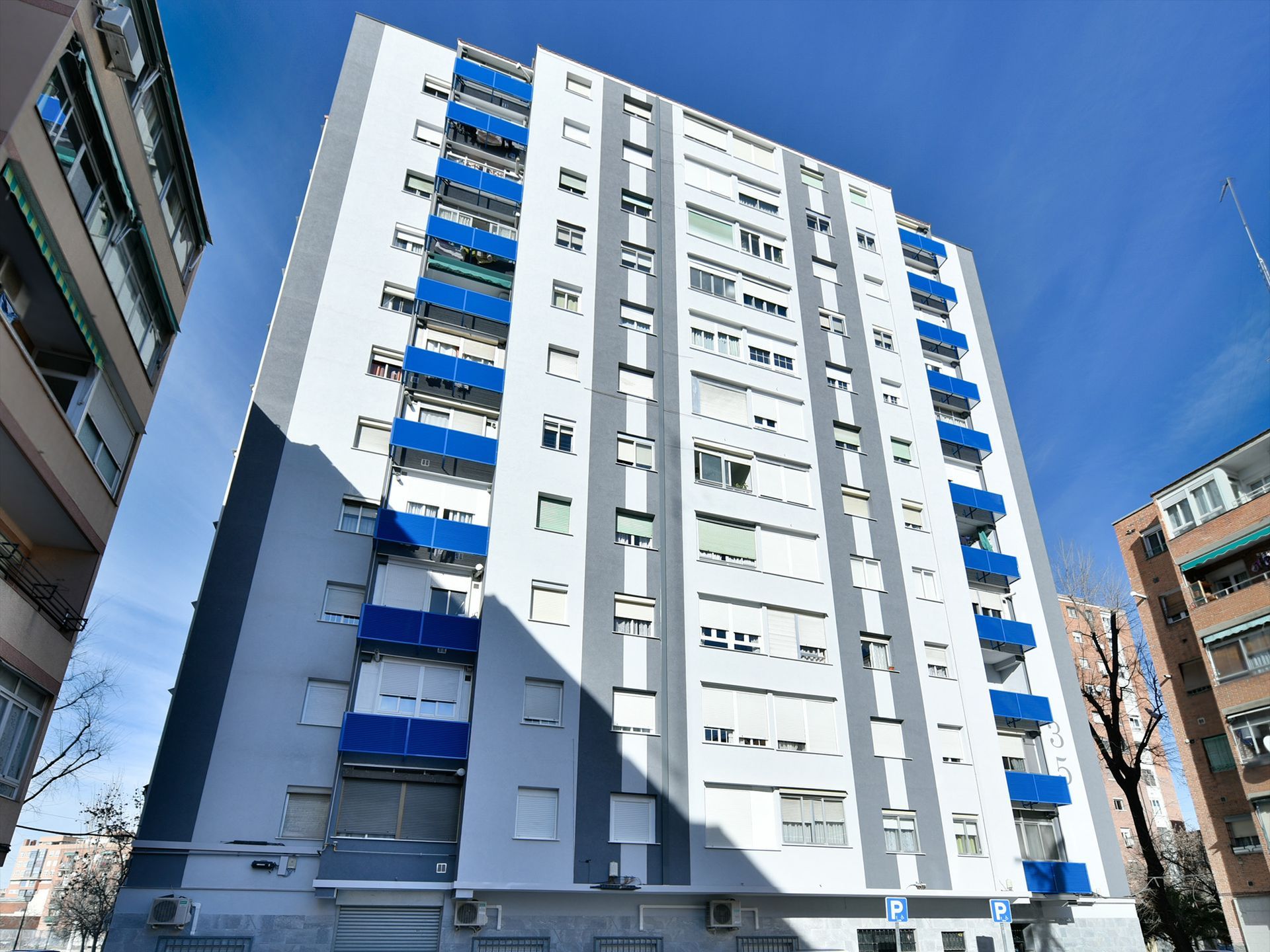 Un edificio blanco con balcones azules está rodeado de otros edificios.