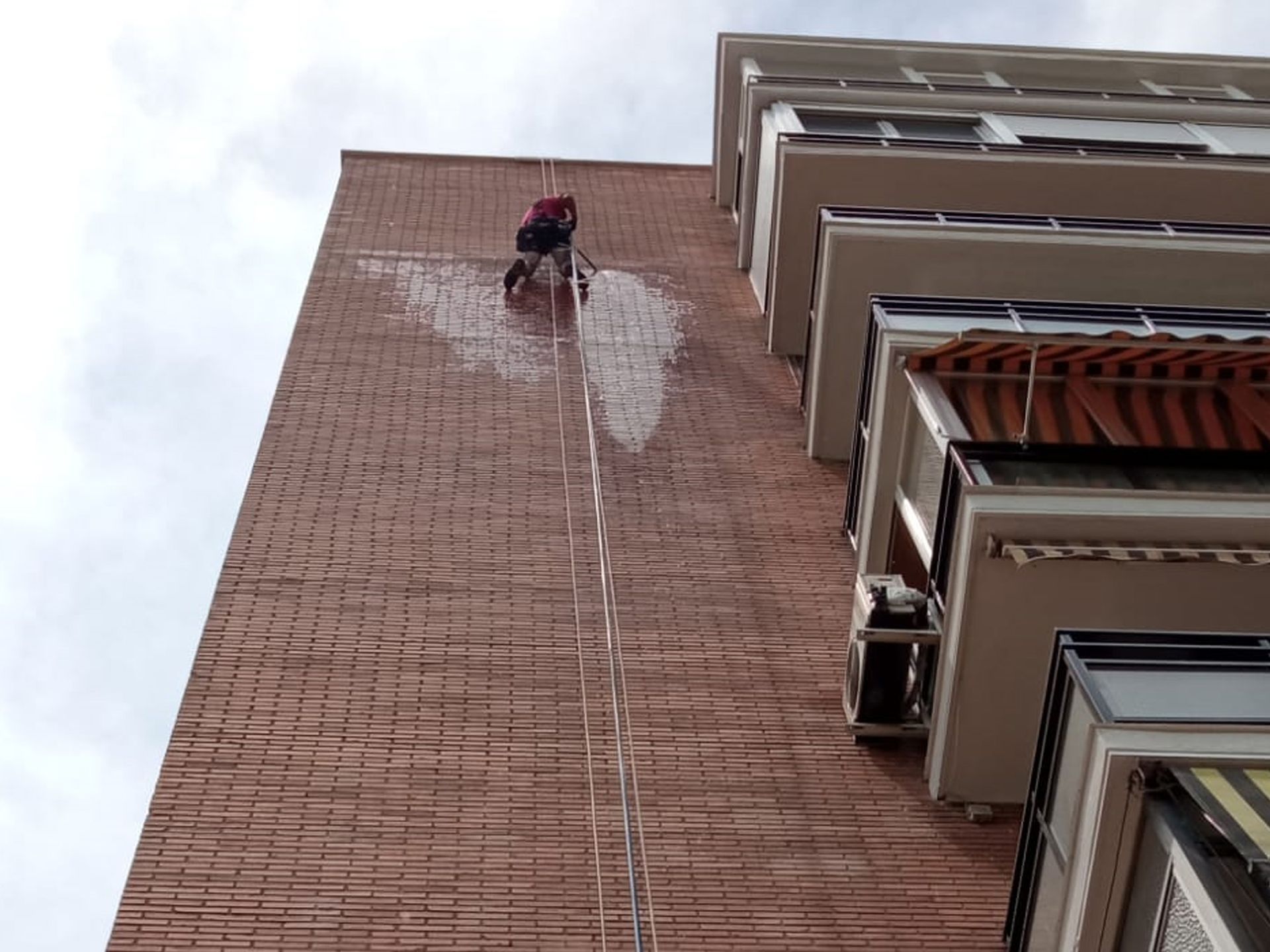Un hombre está limpiando un edificio de ladrillos con una cuerda.