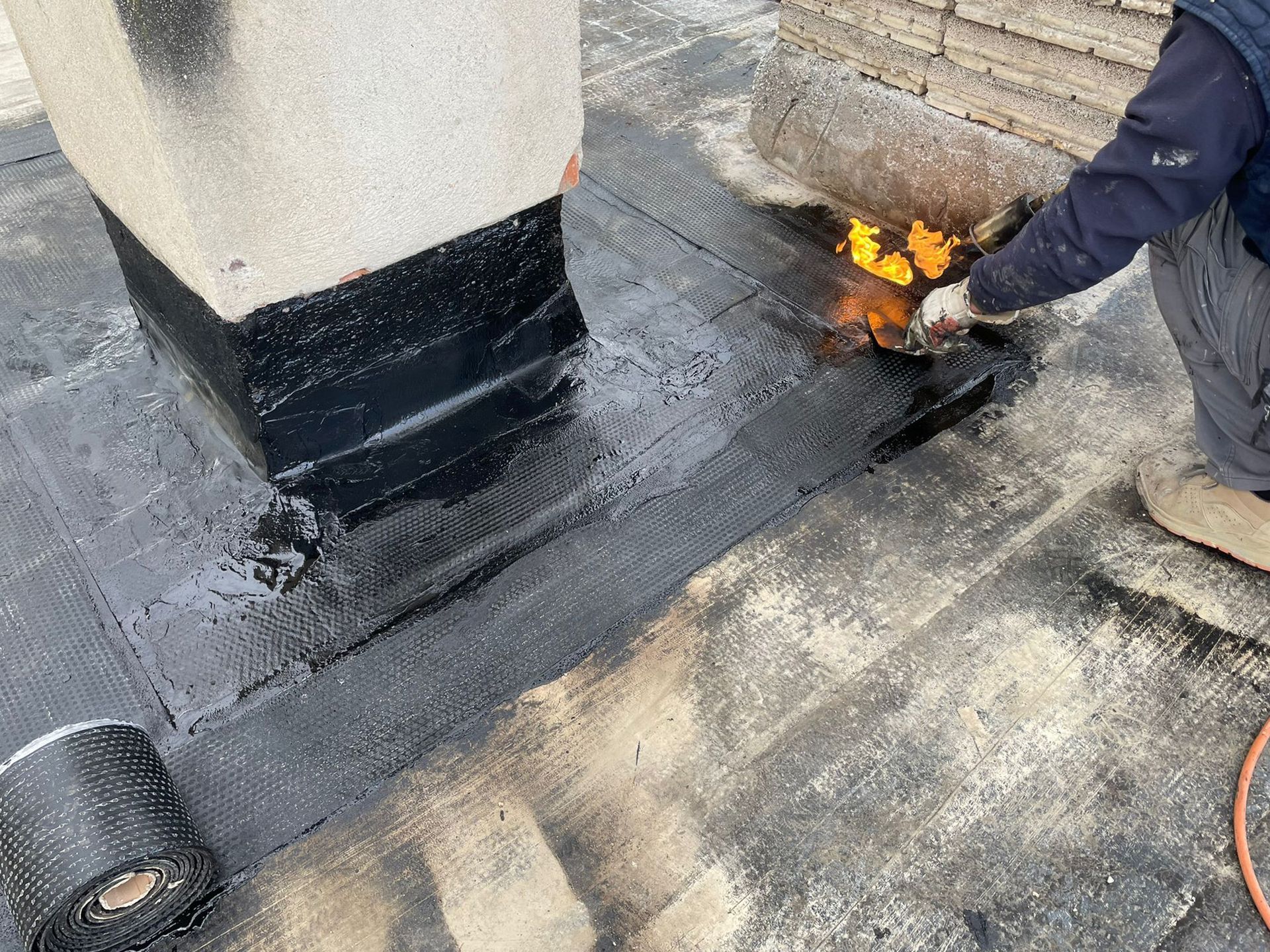 Un hombre está usando una antorcha para calentar un techo.