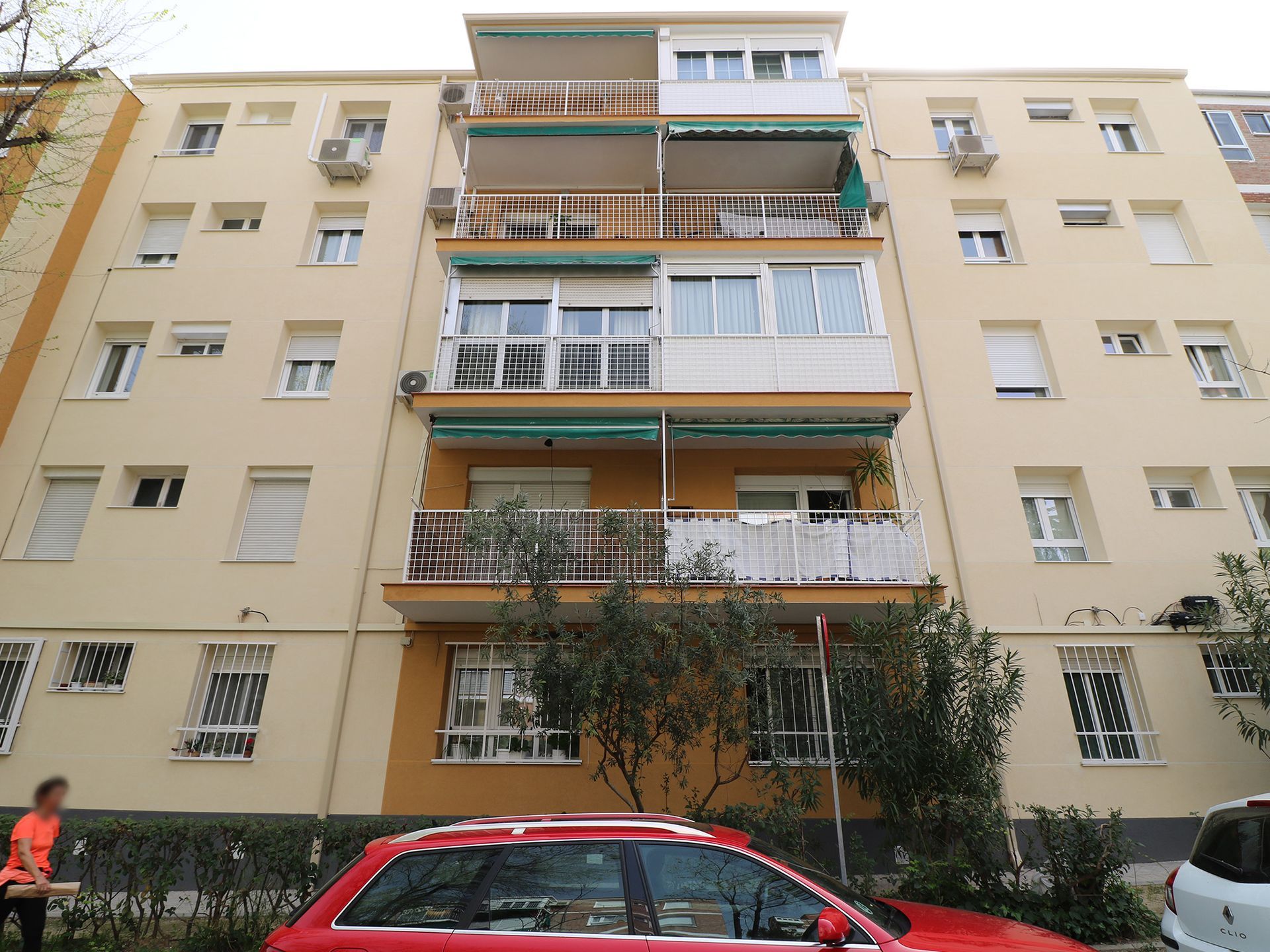 Un coche rojo está aparcado delante de un gran edificio de apartamentos.