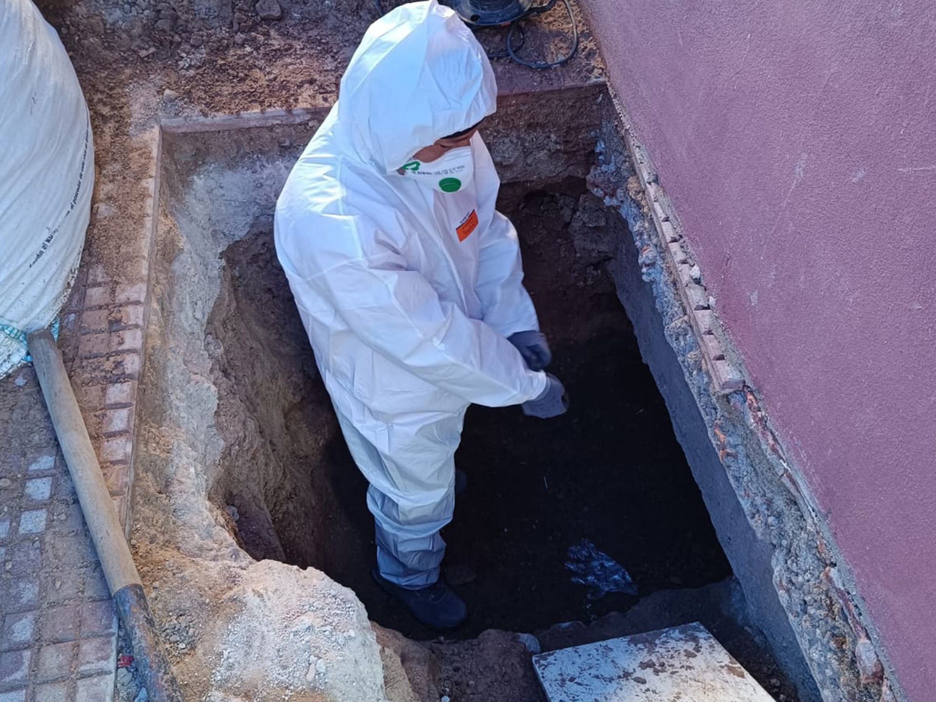 Un hombre con un traje de protección está cavando un hoyo en el suelo.