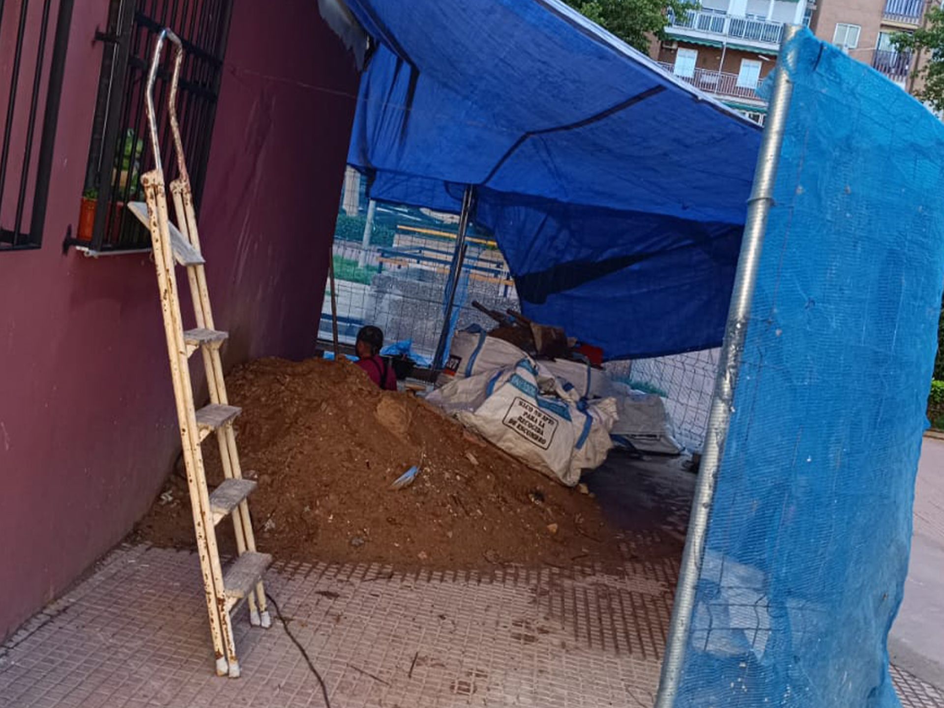Una lona azul cubre un montón de tierra al lado de una escalera.