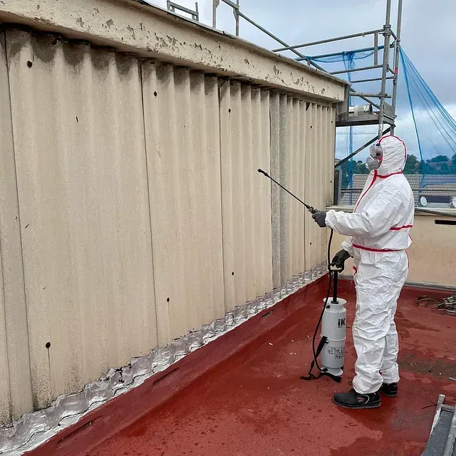 Un hombre con traje protector rociando una pared con un pulverizador.