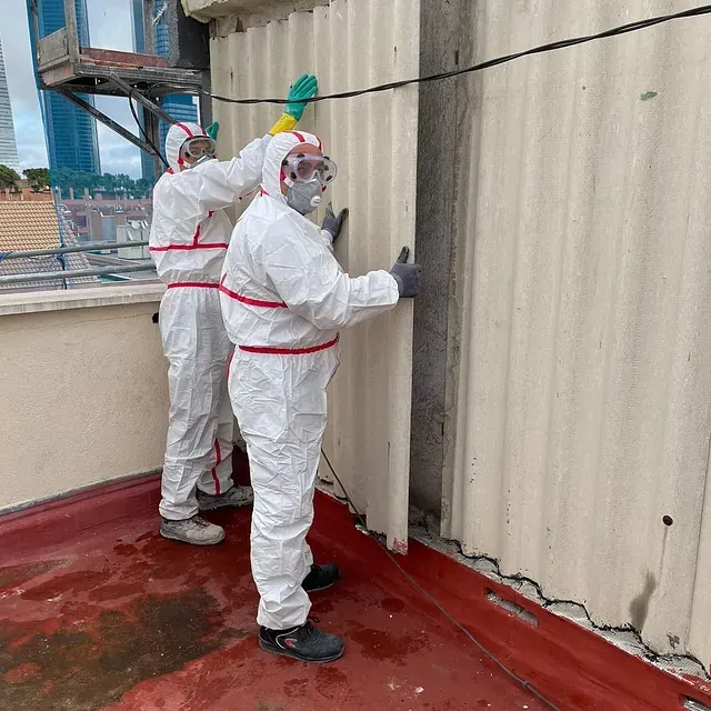 Dos hombres con trajes de protección están trabajando en una pared.