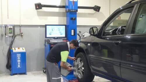 Mecânico alinhando a roda de um carro com o auxílio de um equipamento em uma oficina.