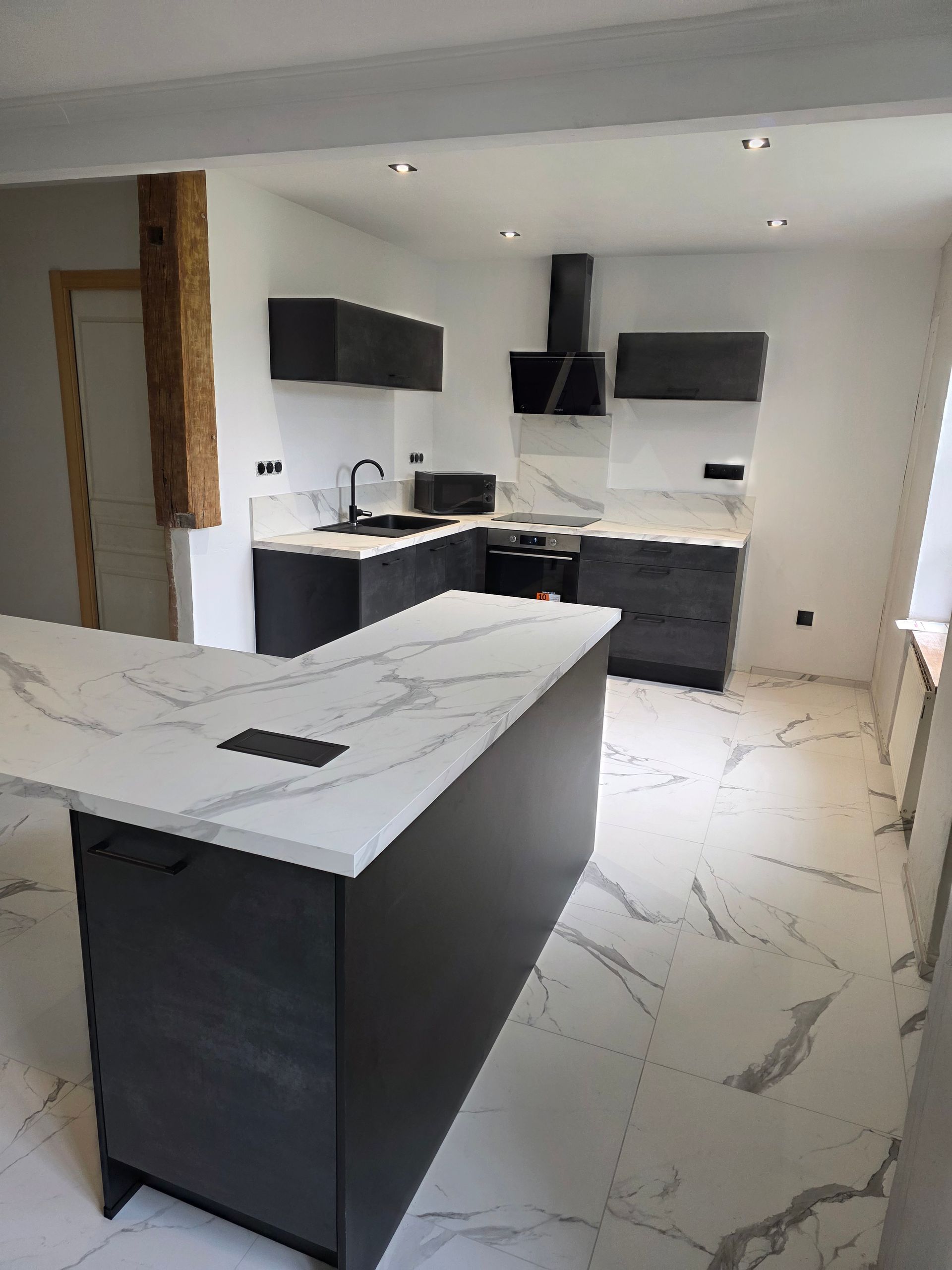Cuisine moderne avec armoires gris foncé, comptoirs en marbre blanc et îlot central.
