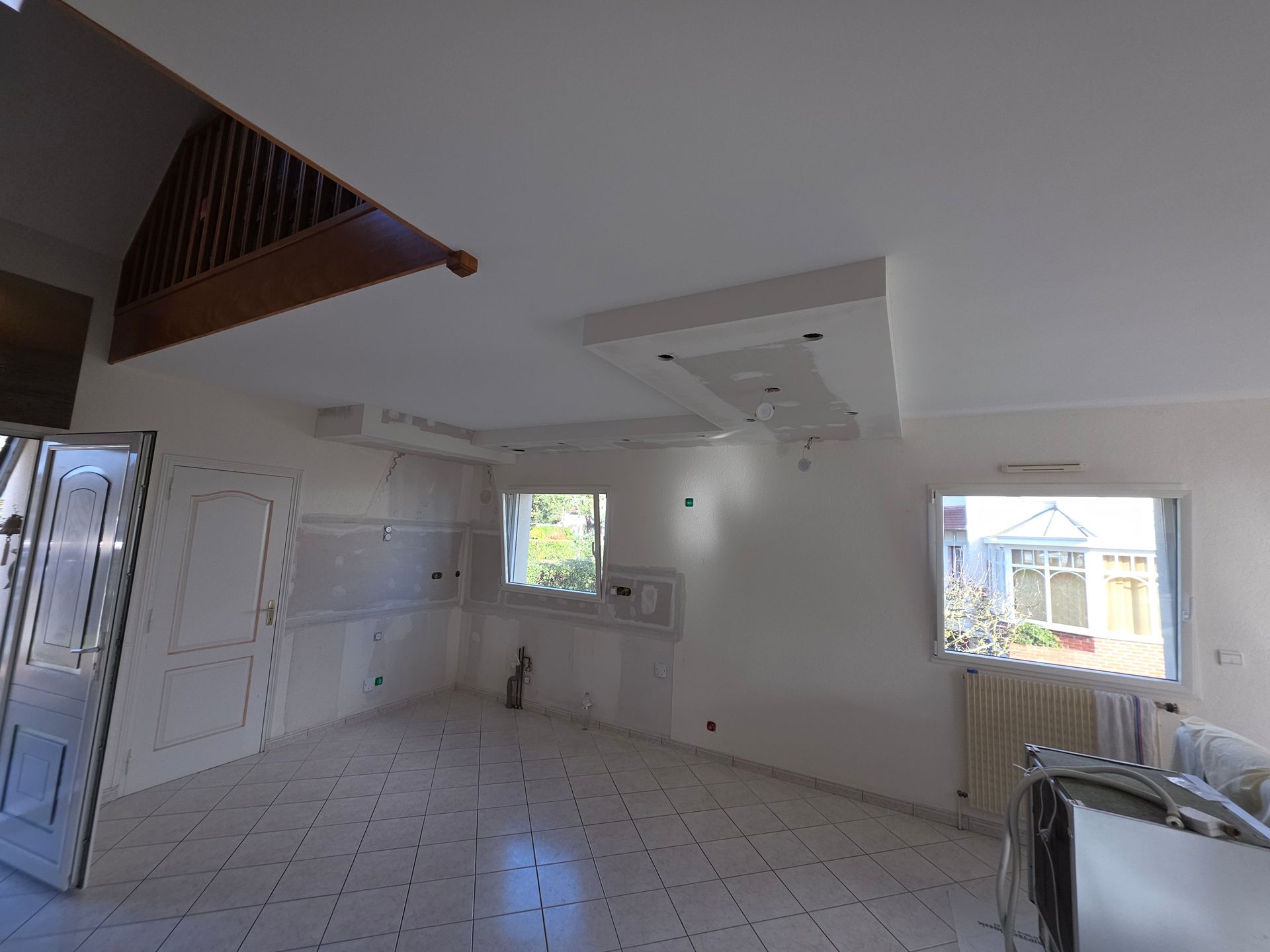 Pièce intérieure en cours de rénovation, avec des plaques de plâtre sur le mur du fond et l'encadrement de la porte, et des débris au sol.