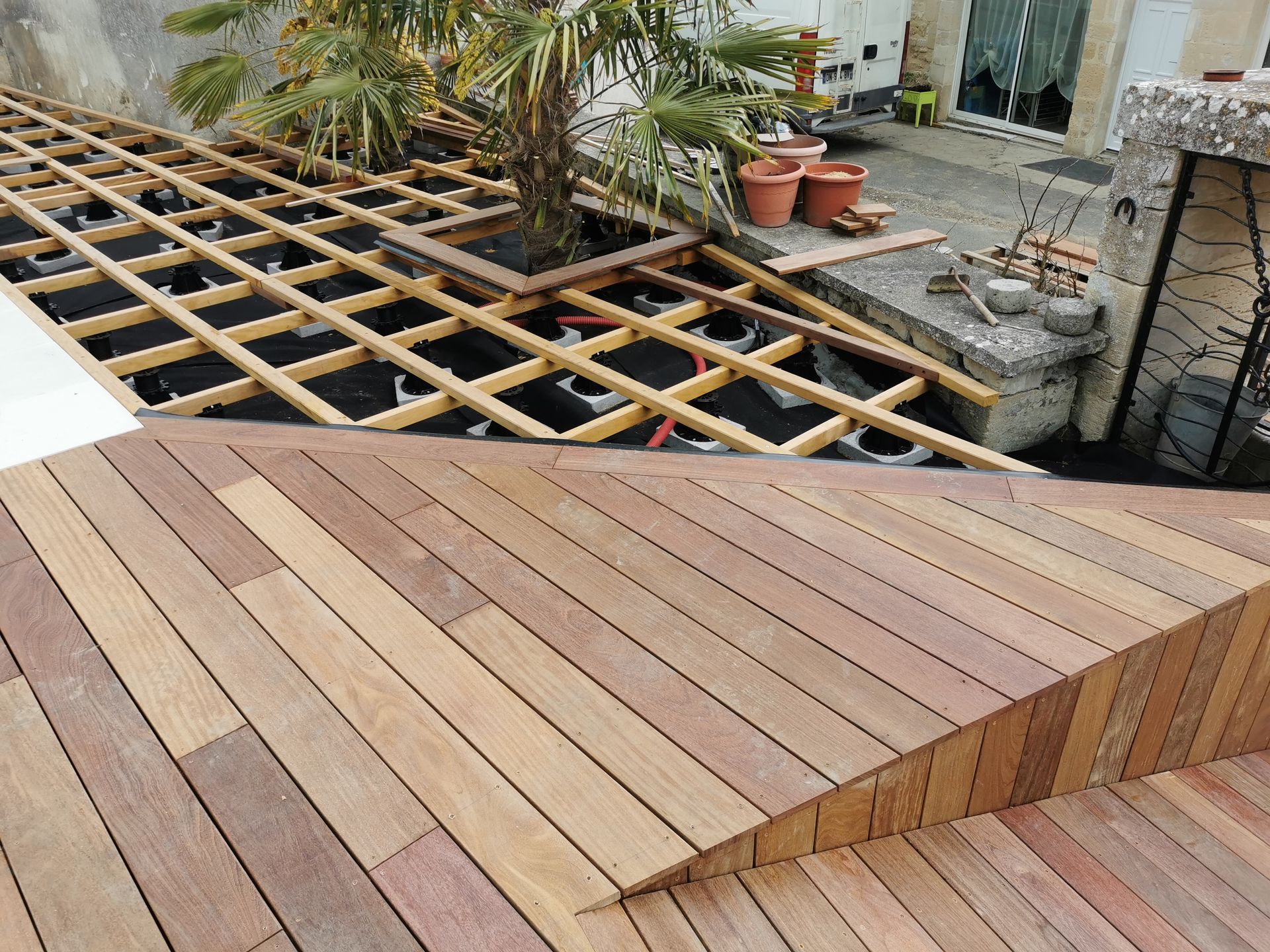 Terrasse en bois en construction, à plusieurs niveaux, entourant un arbre et une jardinière.