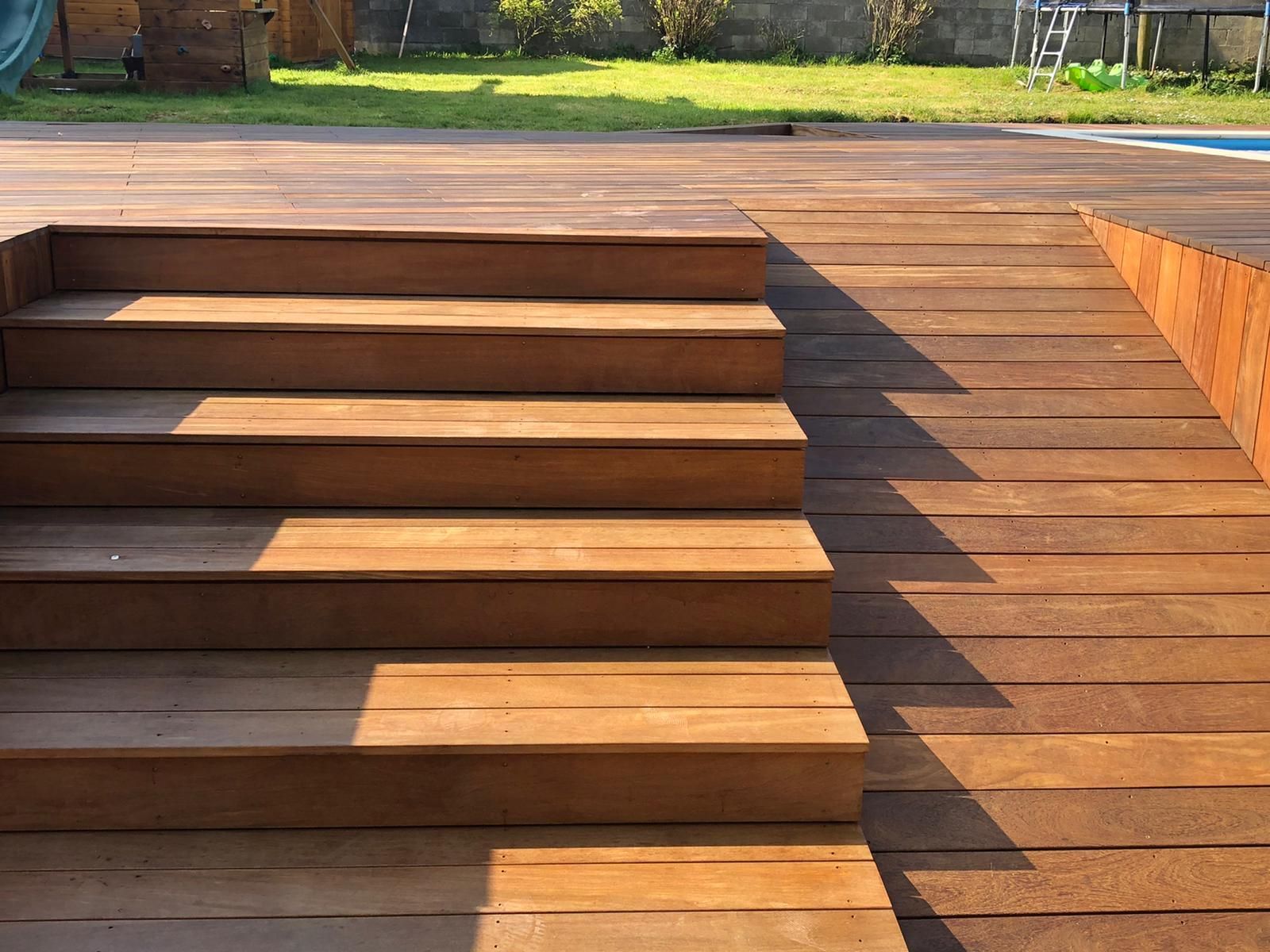 Des marches et une rampe en bois mènent à la terrasse d'une piscine par une journée ensoleillée.