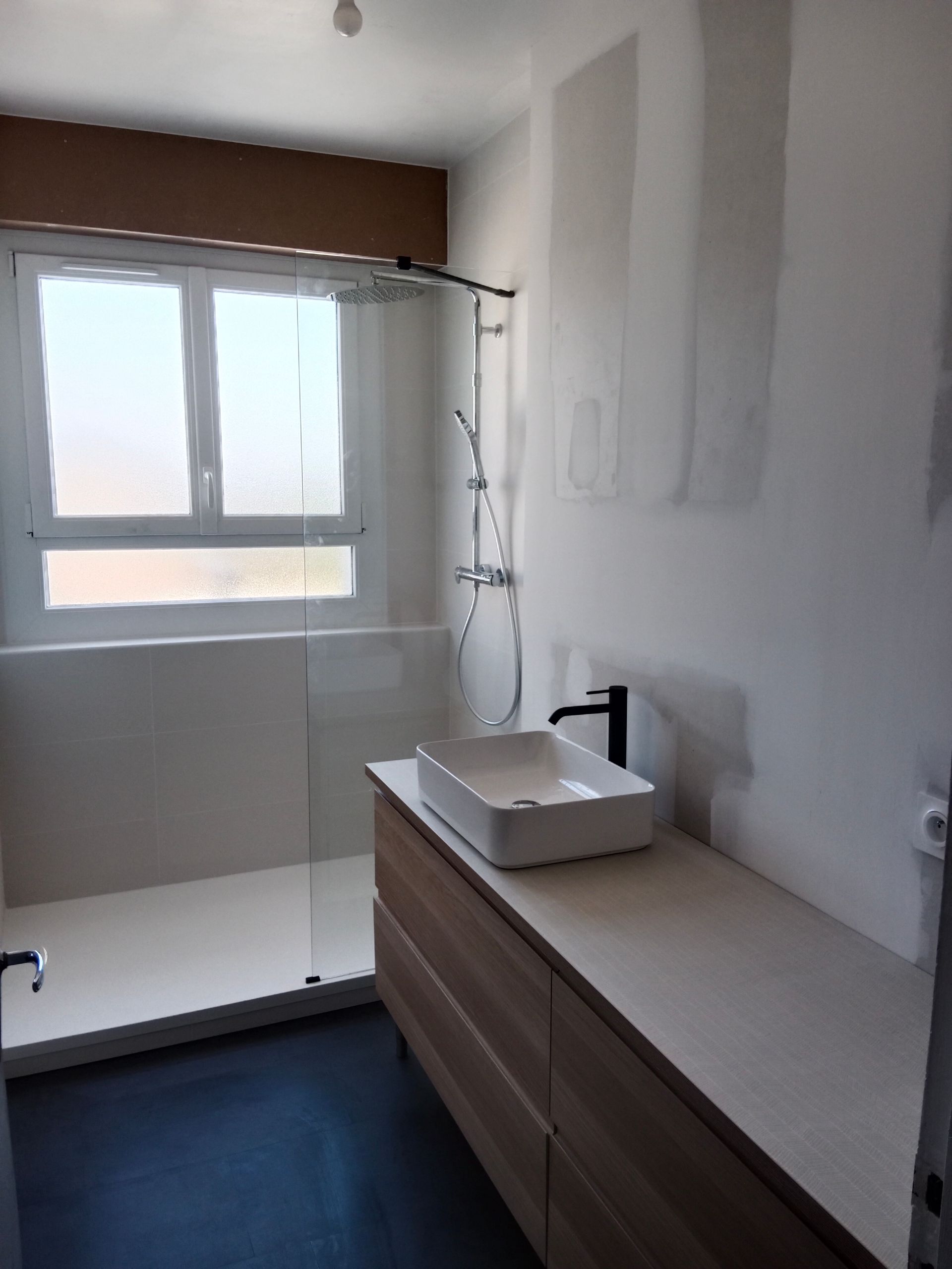 Salle de bains moderne avec douche, meuble lavabo avec vasque et fenêtre.