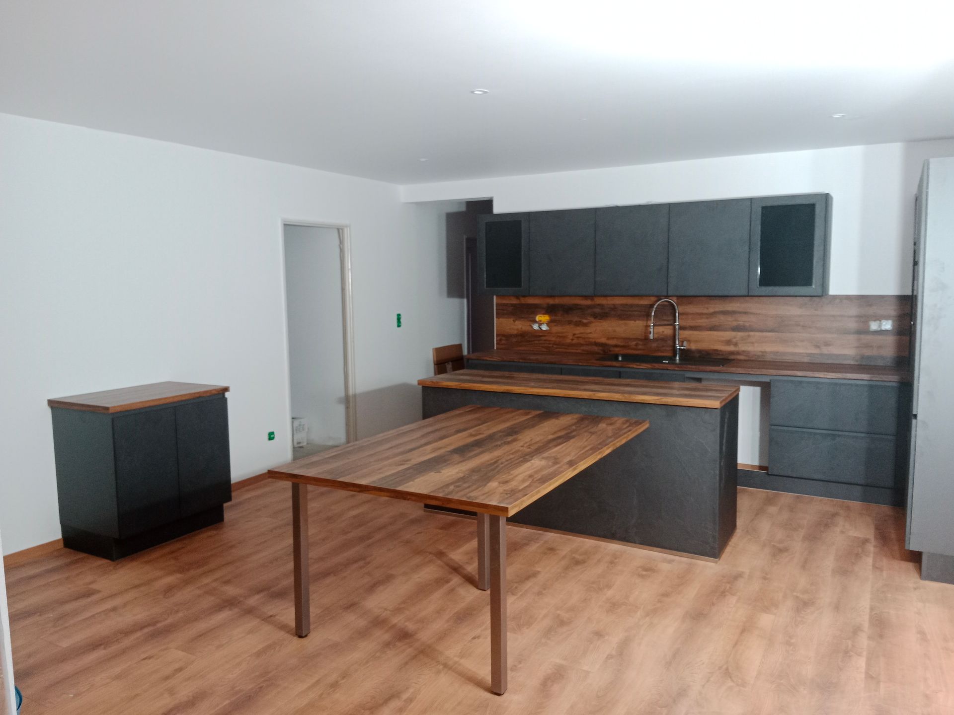 Cuisine moderne avec placards foncés, plans de travail et sol en bois et une table à manger.