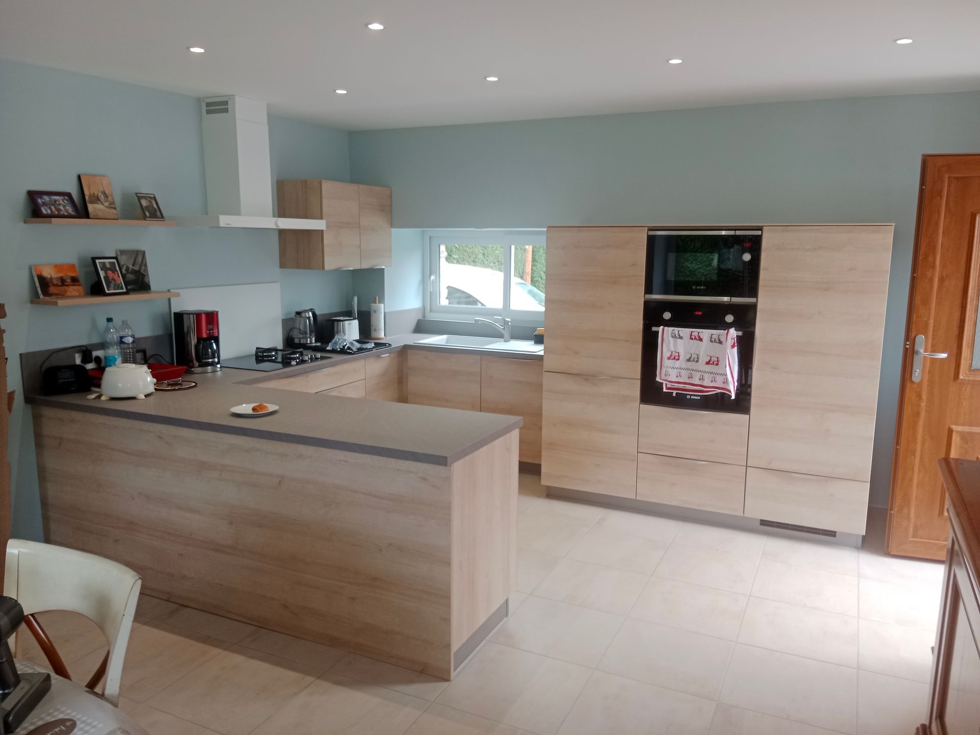 Cuisine moderne avec placards en bois clair, plans de travail gris et murs bleus.