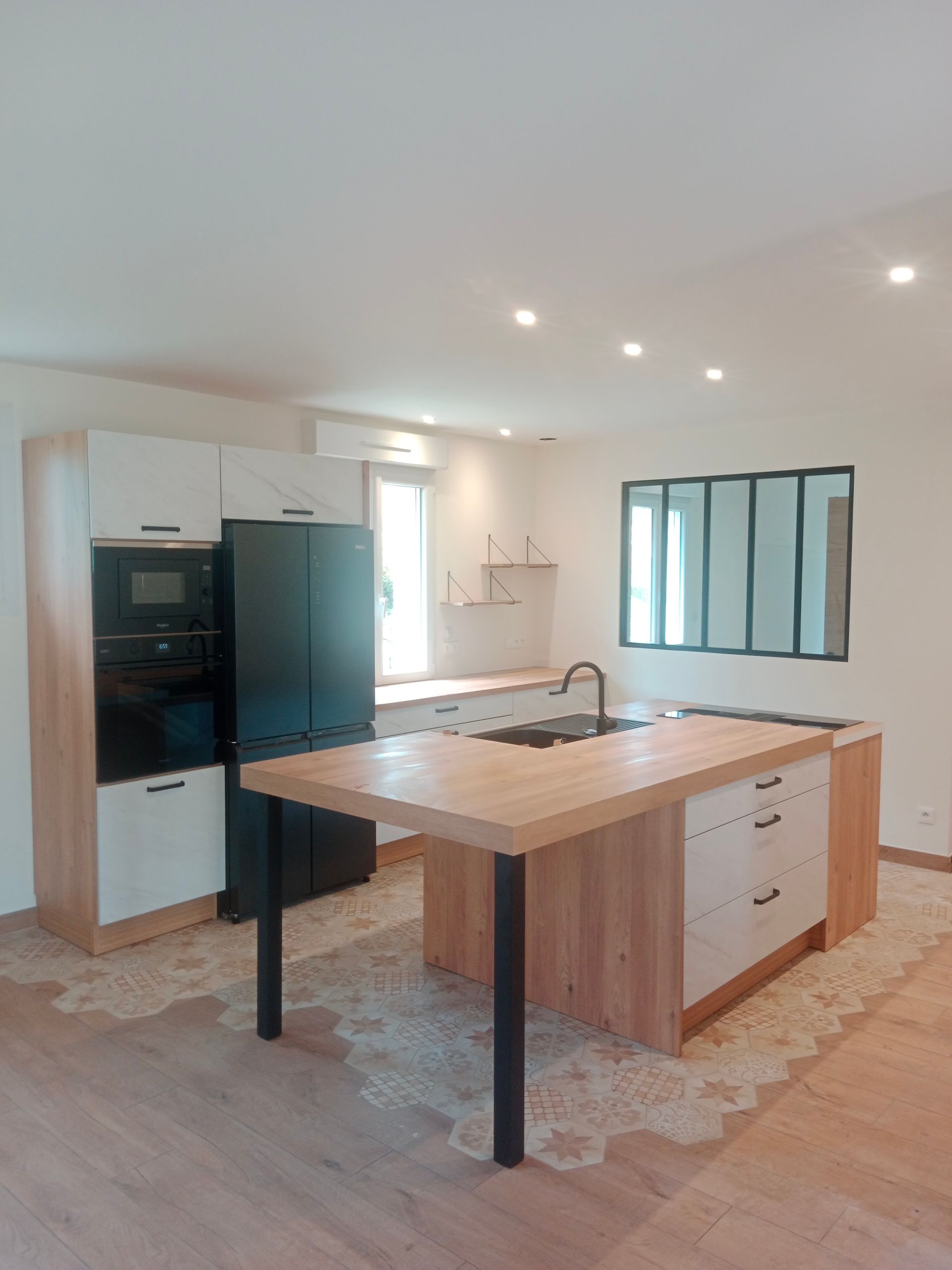 Cuisine moderne avec îlot central, réfrigérateur noir, placards blancs et éléments en bois.