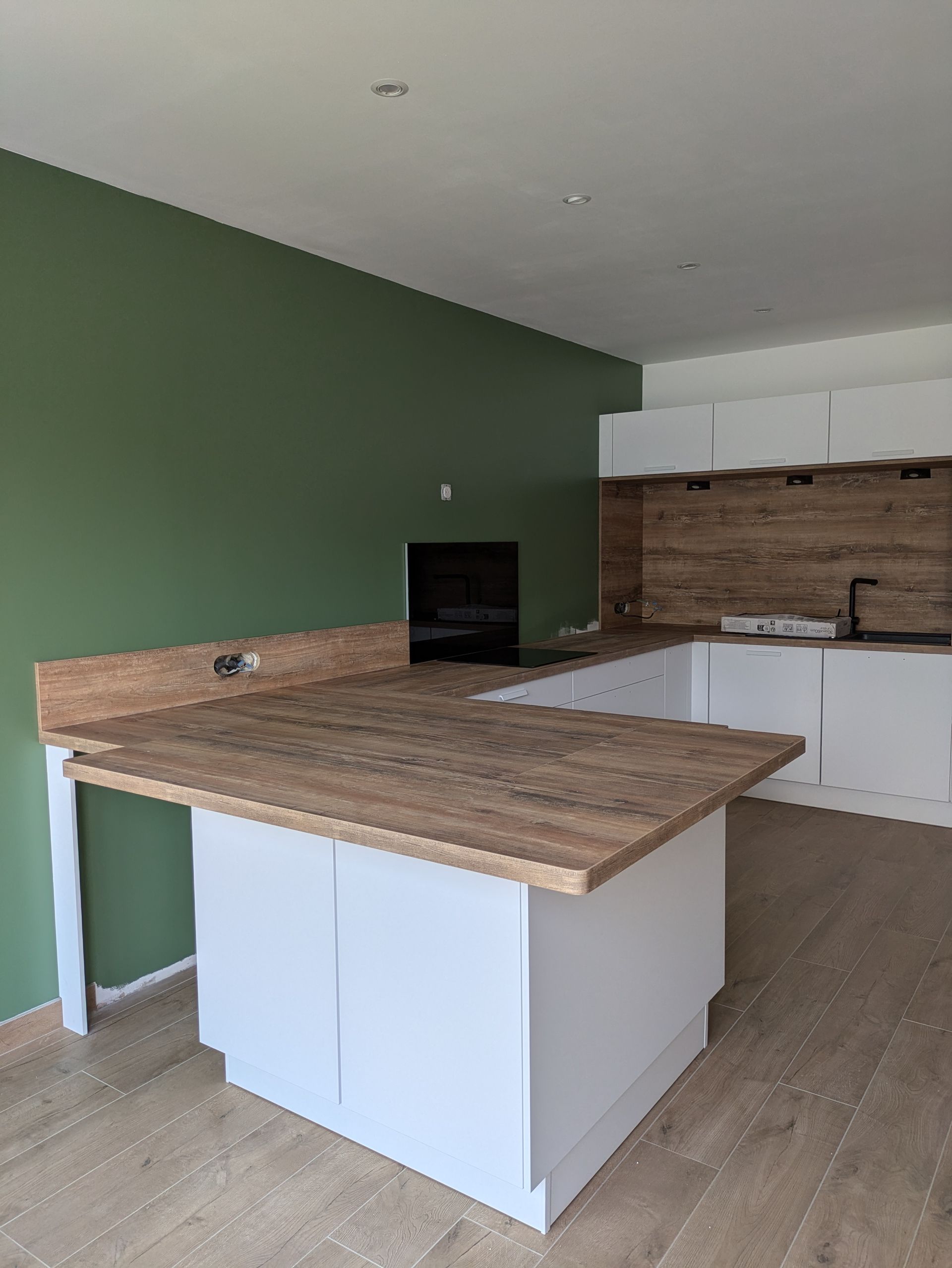 Cuisine moderne avec placards blancs, plan de travail en bois et mur vert olive.